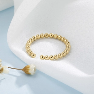 Détail de la bague à perles dorées minimaliste sur un tissu blanc texturé