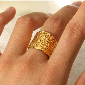 Close-up of a wide gold ring with a hammered texture on a woman's index finger
