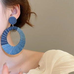 Close-up of stylish oval denim fabric cutout earrings on model with fabric texture detail