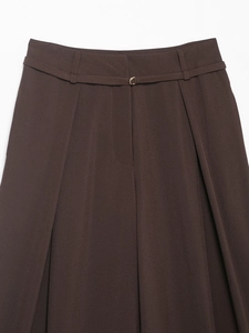 Dettaglio dei pantaloni larghi marrone scuro con cintura sottile e fibbia dorata