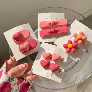 Close-up of pink heart, flower, and bow hair clips on white cardboards in a glass plate