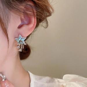 Close-up of star-shaped silver drop earrings with blue zircon on female model