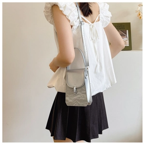 Silver metallic textured shoulder bag worn with a white blouse and black pleated skirt