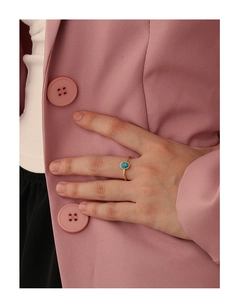 Detail of bohemian gold ring with oval turquoise stone worn on hand against pink blazer