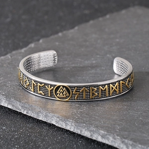 Nordic Viking rune open bangle in silver and gold finish on a dark stone background