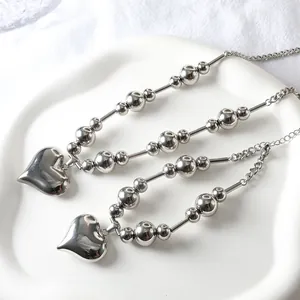 Detail of silver steel bead chains with polished heart pendants on white ceramic