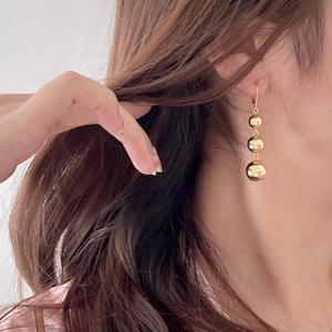 Close-up of a model wearing minimalist triple gold sphere drop earrings in silver