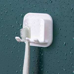 White wall-mounted plastic toothbrush holder on dark green background with water droplets