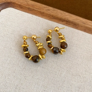 Detail view of golden hoop earrings with tiger eye beads on a natural linen background