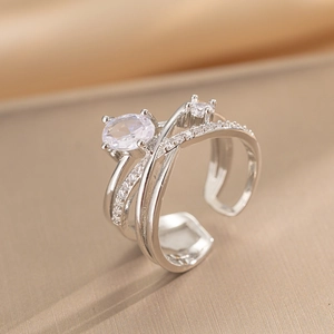 Crossed silver open ring with multi-layer cubic zirconia stones on champagne fabric