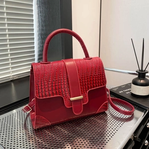 Dunkelrote Lederhandtasche mit Krokostruktur und Goldverschluss auf Metalltablett