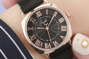 Detailed macro view of woman wearing a black mesh strap quartz watch with Roman numerals