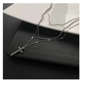 Detailed close-up of a silver triple-layer cross necklace on a modern bicolored background