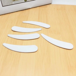 Set of 5 white curved facial cream scoops for cosmetic sampling on a wooden surface