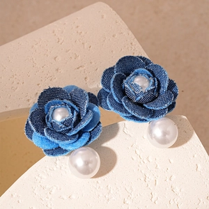 Detail of blue denim flower earrings with pearls on a beige stone background
