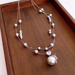 Détail du collier de perles à double rang avec zircon en cœur et charme de couronne