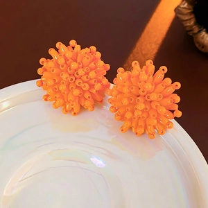 Vibrant orange beaded ball earrings crafted with glossy spheres on an iridescent ceramic plate