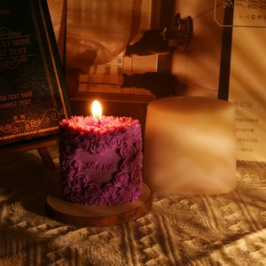 Close-up of a lit purple rose pillar candle with Love engraving on a wooden base