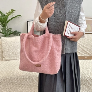 Detail of pink plush tote bag with brown leather brand tag in a cozy home interior setting