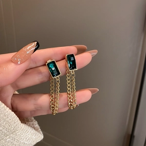 Detail shot of emerald glass gemstone earrings with gold chain fringe on a silver pin base
