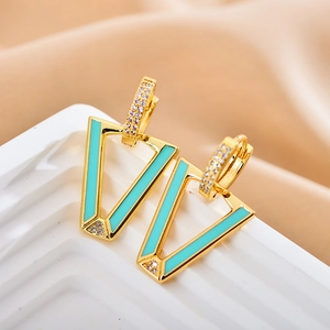 Macro shot of gold V-shaped earrings with green enamel inlay and sparkling rhinestones
