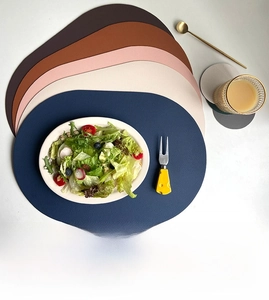 Vertical top view of layered oval faux leather placemats and coasters in various colors
