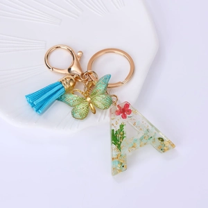 Detail of resin letter A keychain with dried flowers, gold butterfly and blue tassel