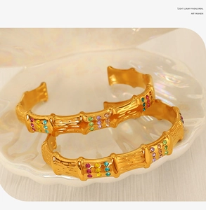 Detail of gold bamboo-shaped bangles with colored crystals resting in a white shell