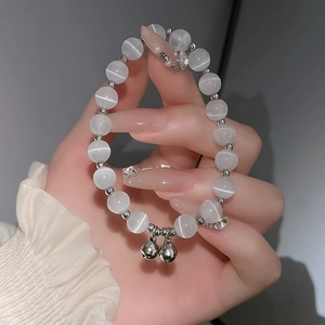 Detail eines Opal-Perlenarmbandes mit Silberglöckchen und Katzenaugeneffekt am Handgelenk