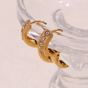 Macro detail of 18K gold-plated twisted hoop earrings with crystals on glass rim
