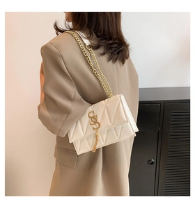 Detailed view of white quilted leather chain bag with gold fringe on a woman's shoulder