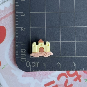 Vue détaillée d'une mini breloque château de sable en résine avec règle de mesure