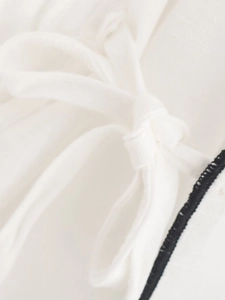 Close-up of white fabric bow tie and black contrast stitching on wide-leg pants