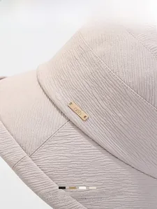 Détail d'un chapeau beige montrant le tricot ondulé et le logo métallique doré