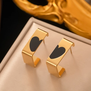 Macro shot of gold C-shaped earrings with black enamel hearts on a beige jewelry cushion