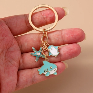 Golden keychain featuring enamel shark, starfish, and stingray charms on a neutral base
