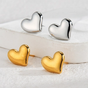 Minimalist 18k gold and silver heart-shaped stud earrings on a white stone base