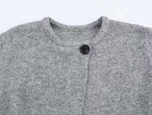 Close-up of gray knit coat neckline with a single black button and textured weave