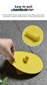 Detail view of yellow silicone drain cover with duck handle and lift tab on gray tiles