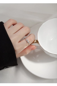 Detail shot of a silver bow knot ring worn by a model holding a white tea cup