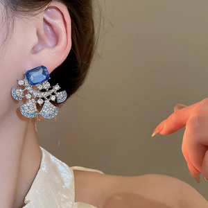 Macro close-up of a luxury floral drop earring with deep blue stone on model