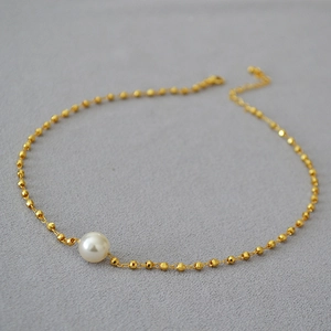 Detail showing laser-cut gold beads and a large lustrous white pearl on a gold necklace