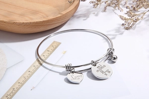 Detail of silver heart charm with Love engraving and mi mama pendant on steel bracelet