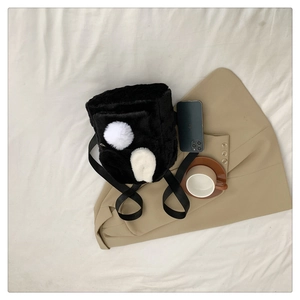 Flat lay of black plush backpack with white pom-poms on a blazer and decorative coffee