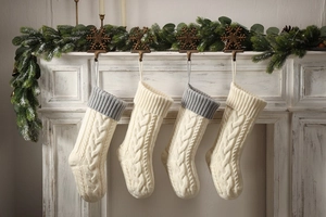 Detail of cable knit Christmas stockings in cream and grey hanging on a white mantel
