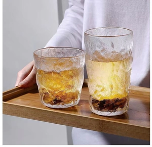 Detail of two glacier textured glass cups with amber liquid on a wooden tray