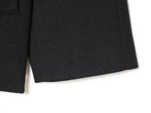 Close-up of the black fabric texture and thick woven cuff detail on a short fashion coat