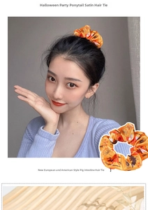Detail of an orange satin Halloween scrunchie with pumpkin and bat prints worn in hair