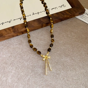 Detailed macro view of tiger eye stone necklace with gold bow pendant on wood frame
