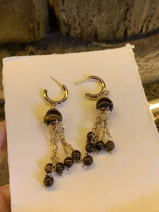 Detail of golden tassel earrings with dark beads and fine chains on white surface